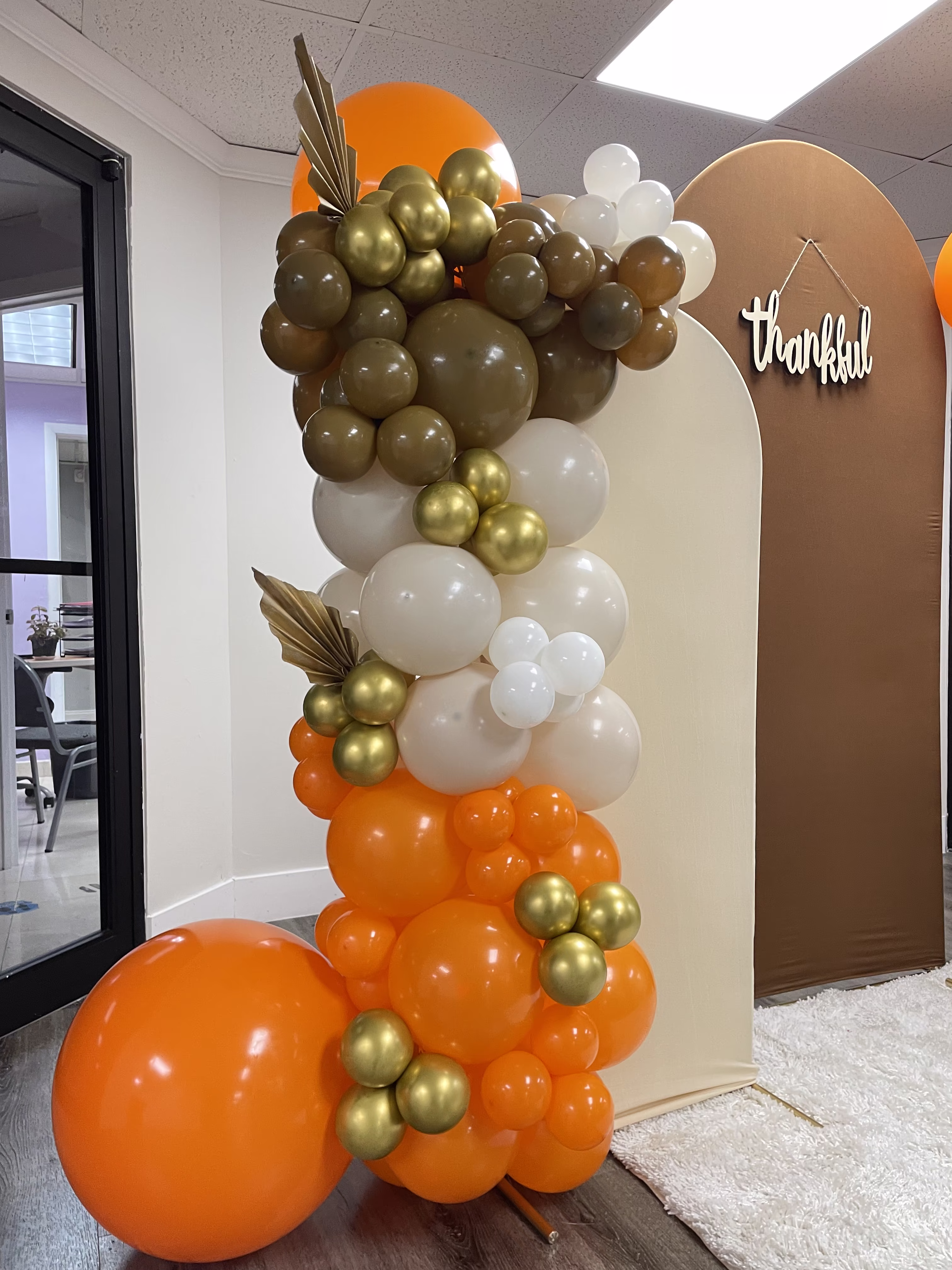 Columna de globos en tonos naranja, crema y olivo con hojas de palma secas